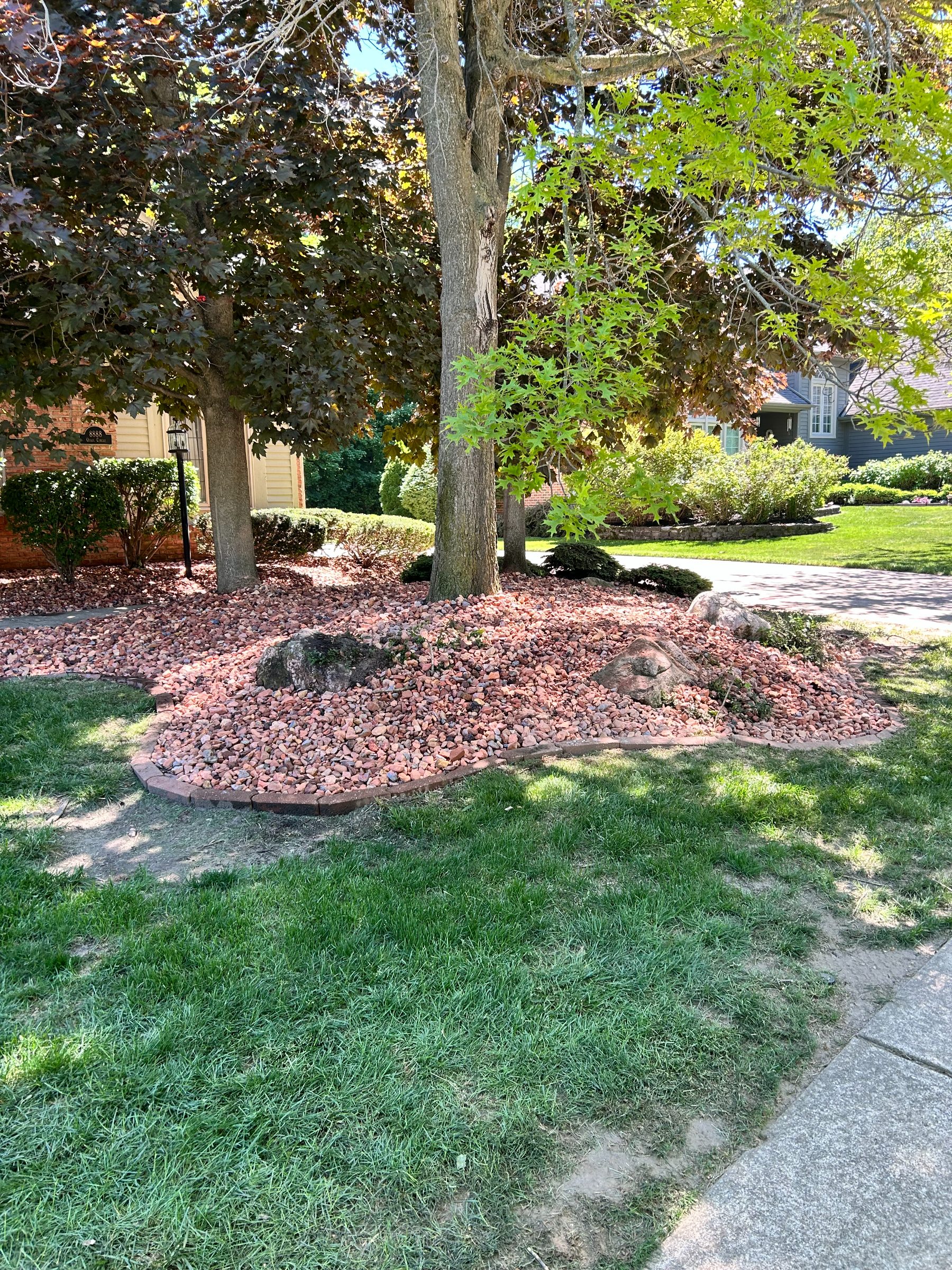 Decorative red rock bed installed in a landscaping bed under mature trees
